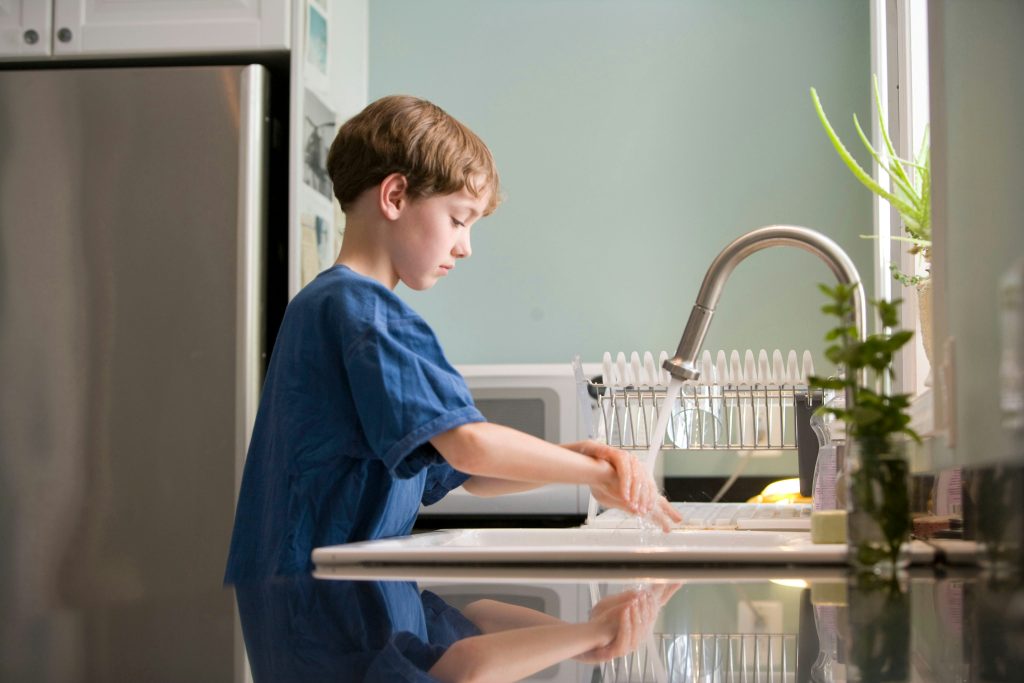 Young boy washing hands with running water at a kitchen sink, promoting hygiene and clean water safety at home.