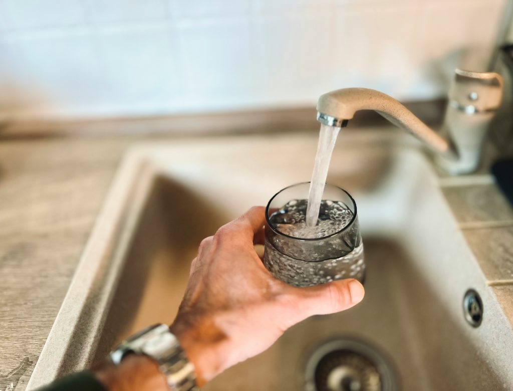 A person fills a glass with water from the kitchen tap, highlighting the need for safe, filtered drinking water