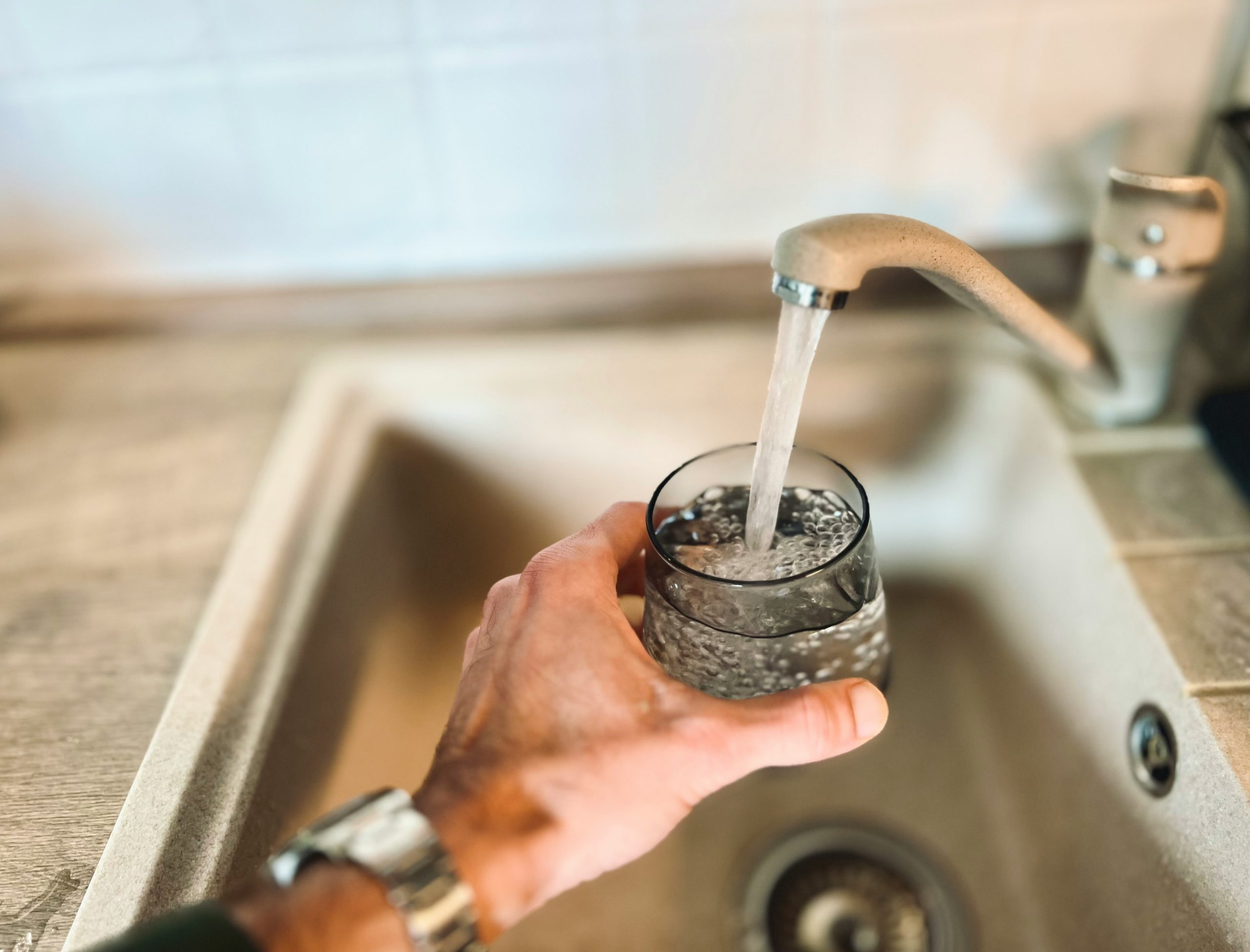A person fills a glass with water from the kitchen tap, highlighting the need for safe, filtered drinking water