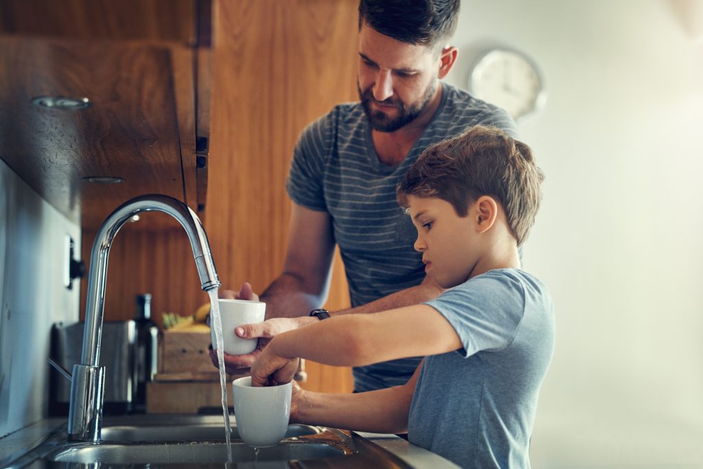 Father and son filling cups with filtered Brita Pro water at the kitchen sink, promoting safe drinking water and family wellness at home.