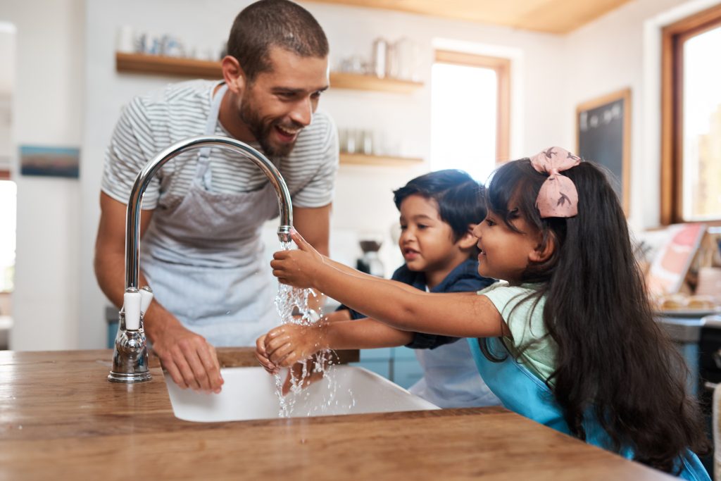 Father teaching his two children proper handwashing at the kitchen sink, highlighting the importance of Brita Pro clean filtered water for safe and healthy family routines.