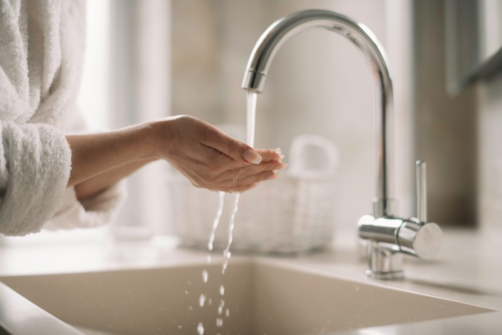 Close-up of a person washing hands with fresh filtered water from a modern kitchen faucet, demonstrating the purity and quality provided by Brita Pro whole-home water filtration systems.