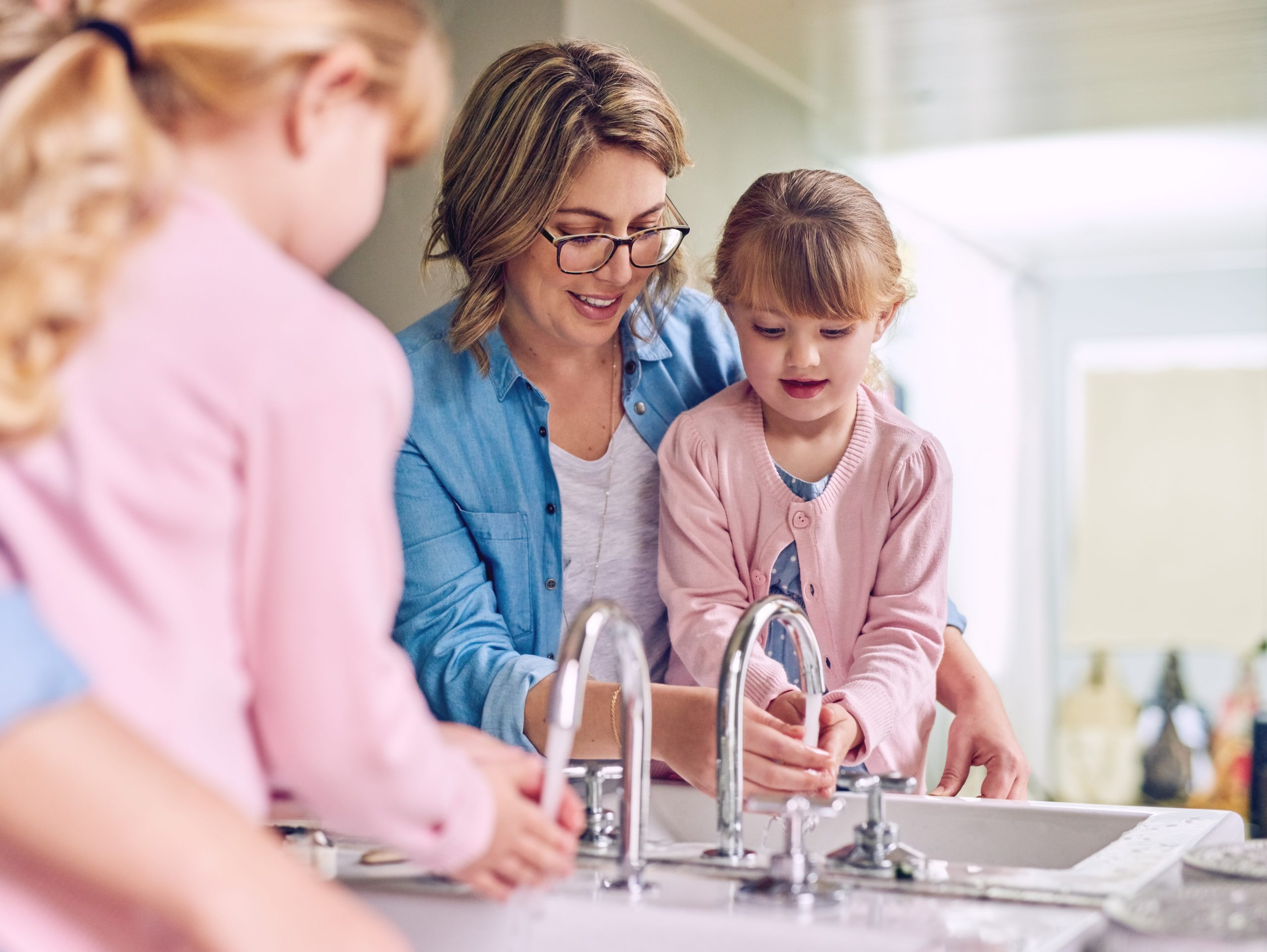 Mother teaching her daughters proper handwashing at the kitchen sink using Brita Pro filtered water, promoting clean water and healthy family habits.