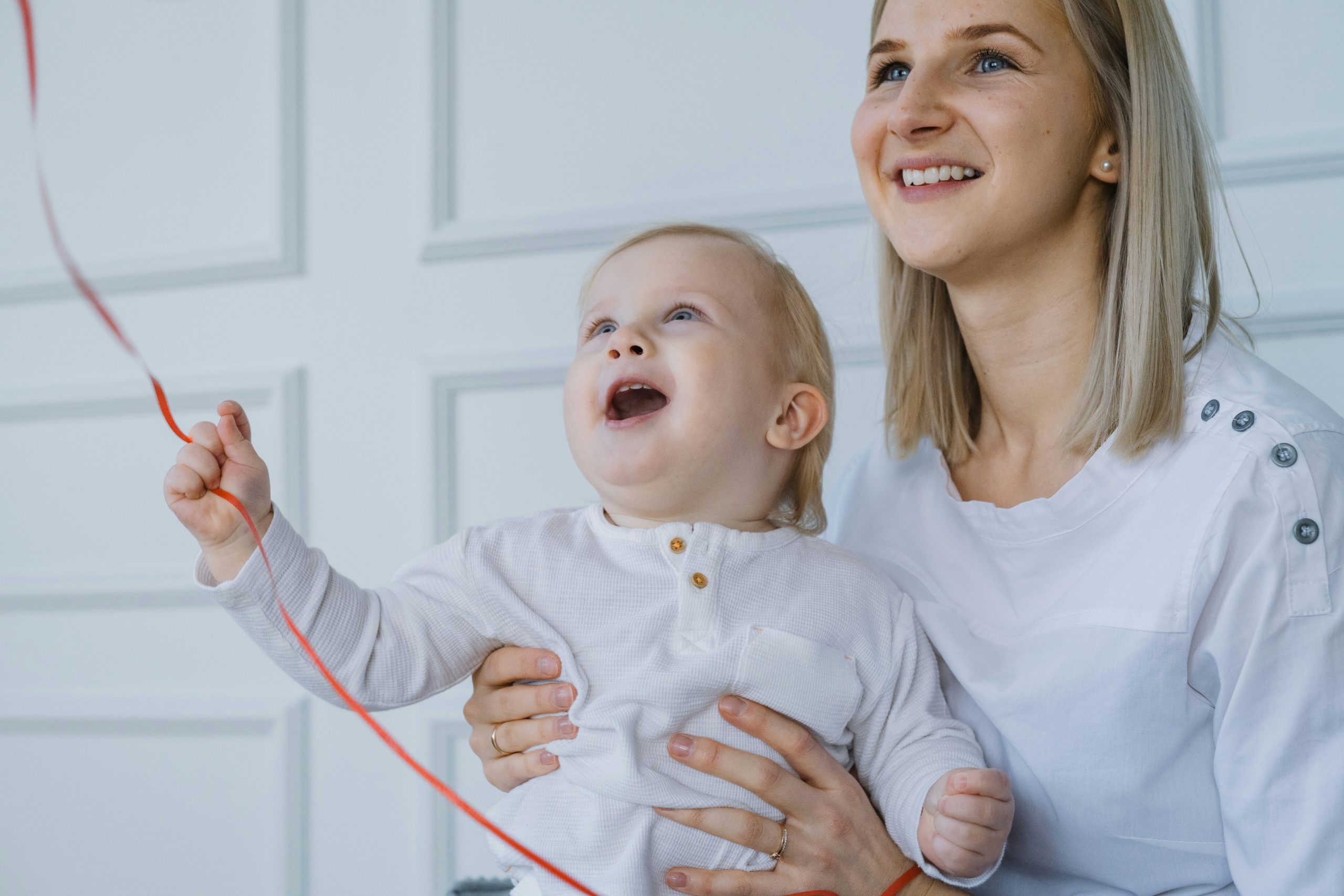 Happy mother and toddler playing indoors with a red ribbon, reflecting a joyful home environment where Brita Pro filtered water supports safe, everyday family moments.