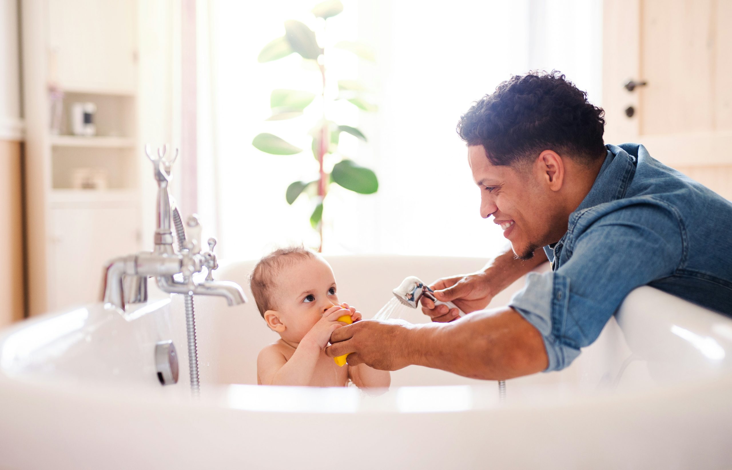 Father giving baby a bath in a bright, modern bathroom, symbolizing the importance of Brita Pro filtered water in protecting delicate skin and enhancing safe family care routines.