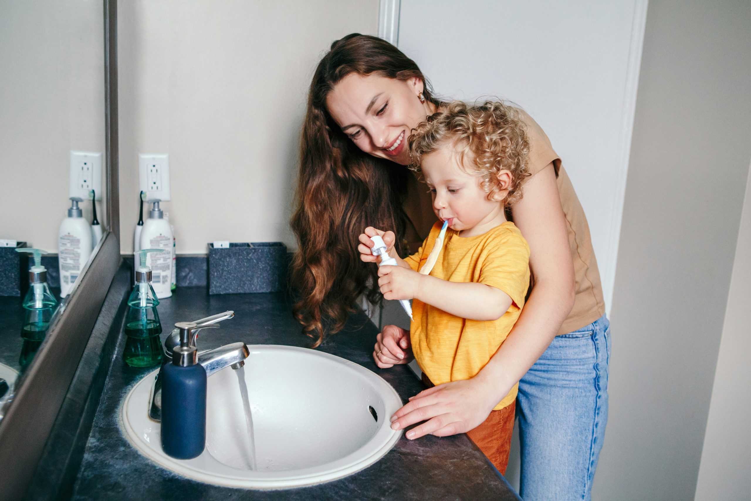 Mother teaching toddler to brush teeth at a bathroom sink, highlighting the role of Brita Pro filtered water in promoting healthy hygiene habits and safe daily routines for young families.