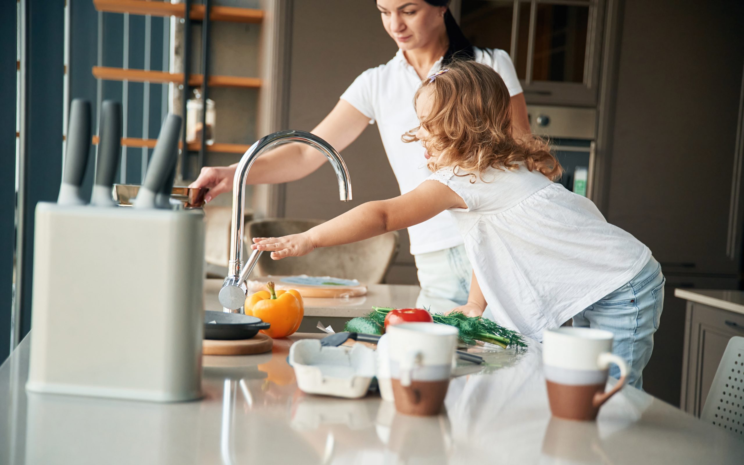 Mother and daughter preparing vegetables in a modern kitchen, using clean, filtered Brita Pro water from the faucet to rinse produce for healthy family cooking.