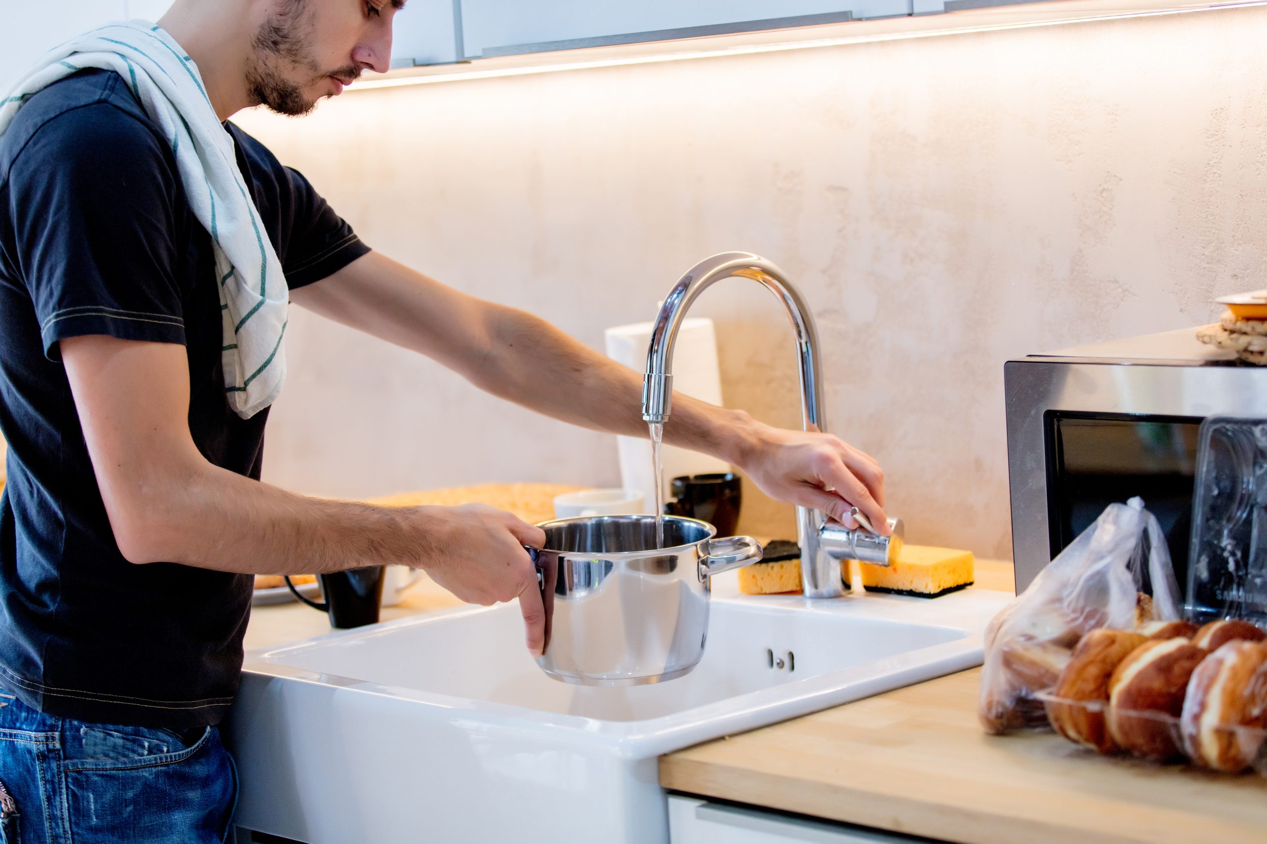 Young man filling a pot with water at the kitchen sink, preparing a meal using clean, filtered Brita Pro water for safe, healthy home cooking.