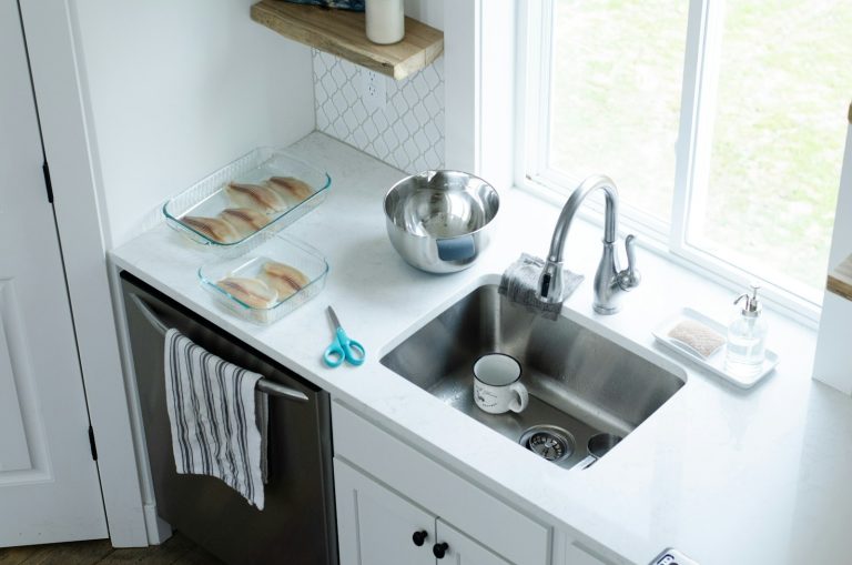 Bright kitchen sink and faucet by a window, where an under-sink reverse osmosis system is installed