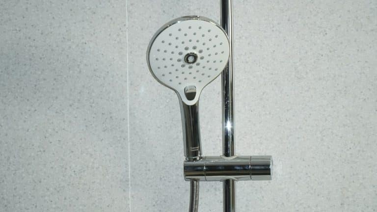 Stainless steel shower head on white tiles, where hard water leaves scale